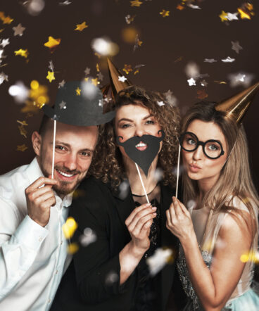 Group of happy people wearing party hats and using funny photo b