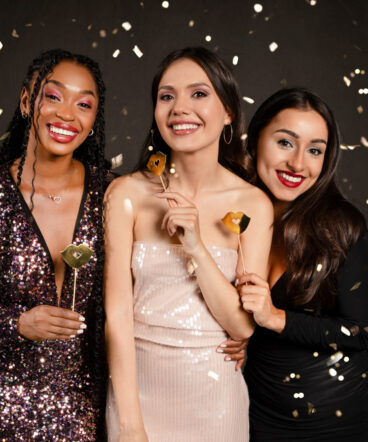 Pretty multiethnic women friends holding photo booth celebrating New Year 2024